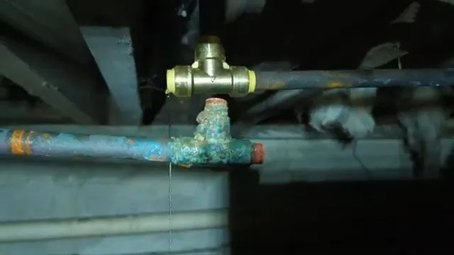 A brass fitting on a pipe with blue-green corrosion, seen from below among floor joists.