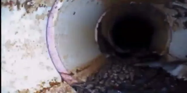 A camera view down a light-colored pipe toward a joint, with grit and debris lying along the bottom.
