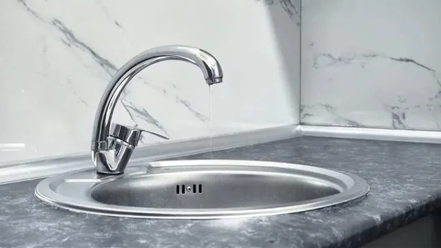 A chrome single-handle kitchen faucet over a round stainless sink with a thin stream of water falling from the spout.