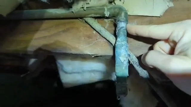 A finger pointing at a green corroded copper elbow in a crawlspace under the floor.