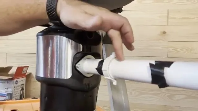 A hand pushing a white dishwasher drain hose onto the side inlet of a garbage disposal.