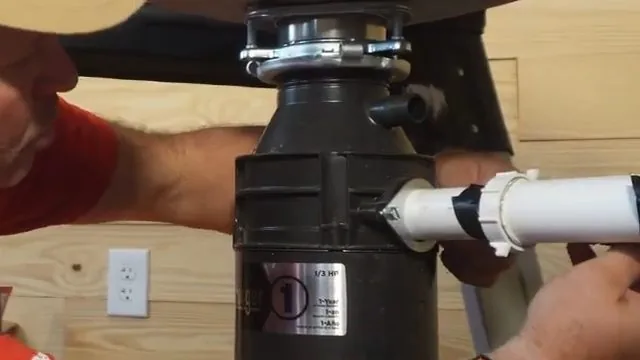 A hand on the white drain pipe where it joins the side of a garbage disposal, held by a clamp and black tape.