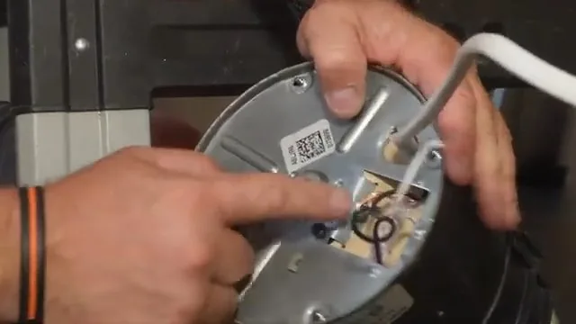 A hand pointing at the wiring compartment under the base plate of a garbage disposal, with a white power cord attached.