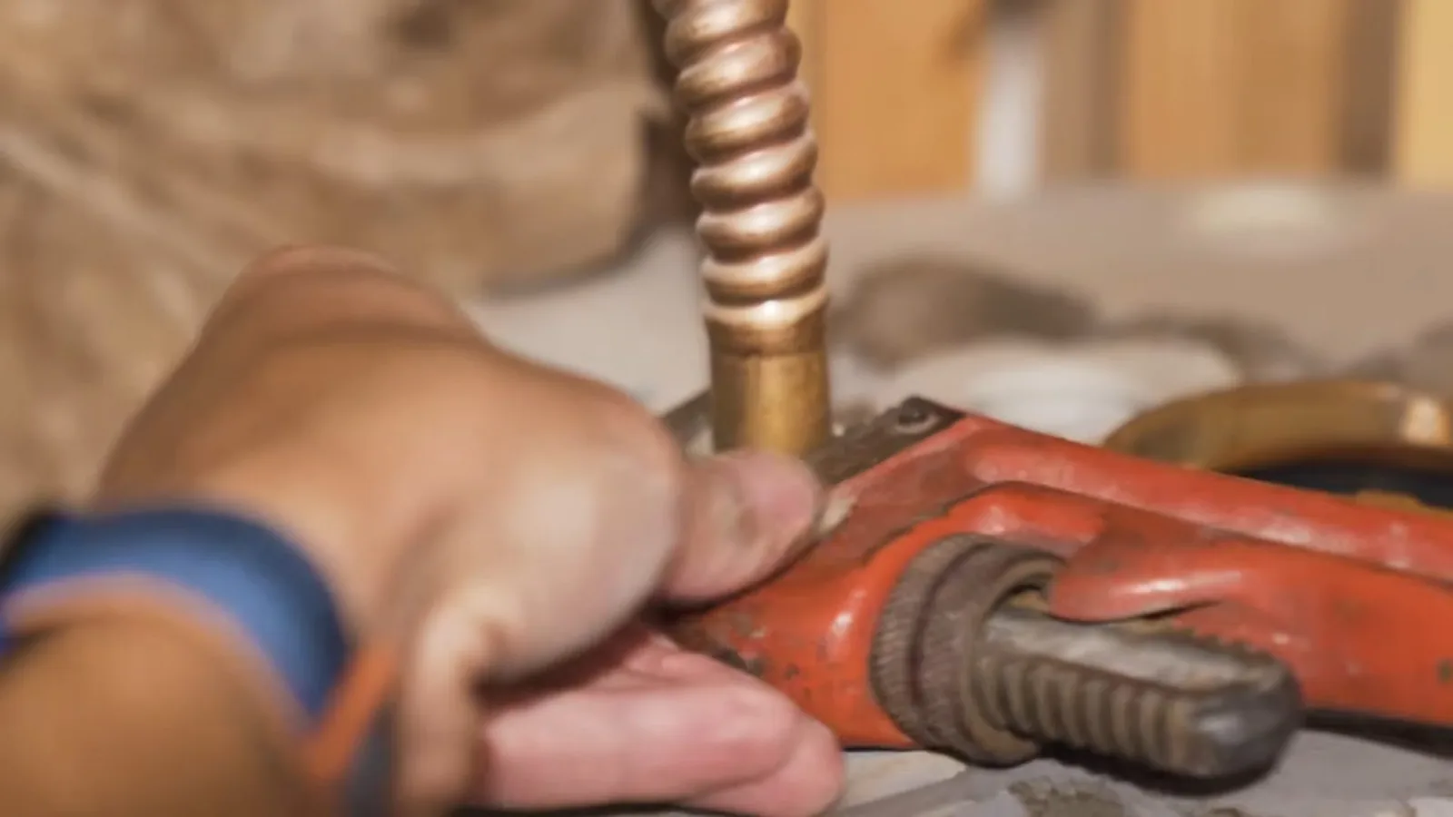 A hand in a work glove turning a red pipe wrench on a corrugated copper connector.