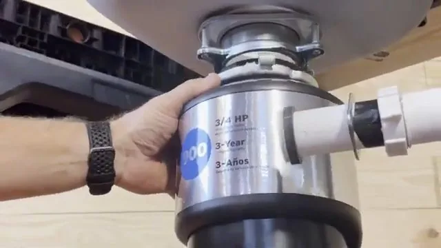 Two hands holding a stainless garbage disposal up against the underside of a sink flange.