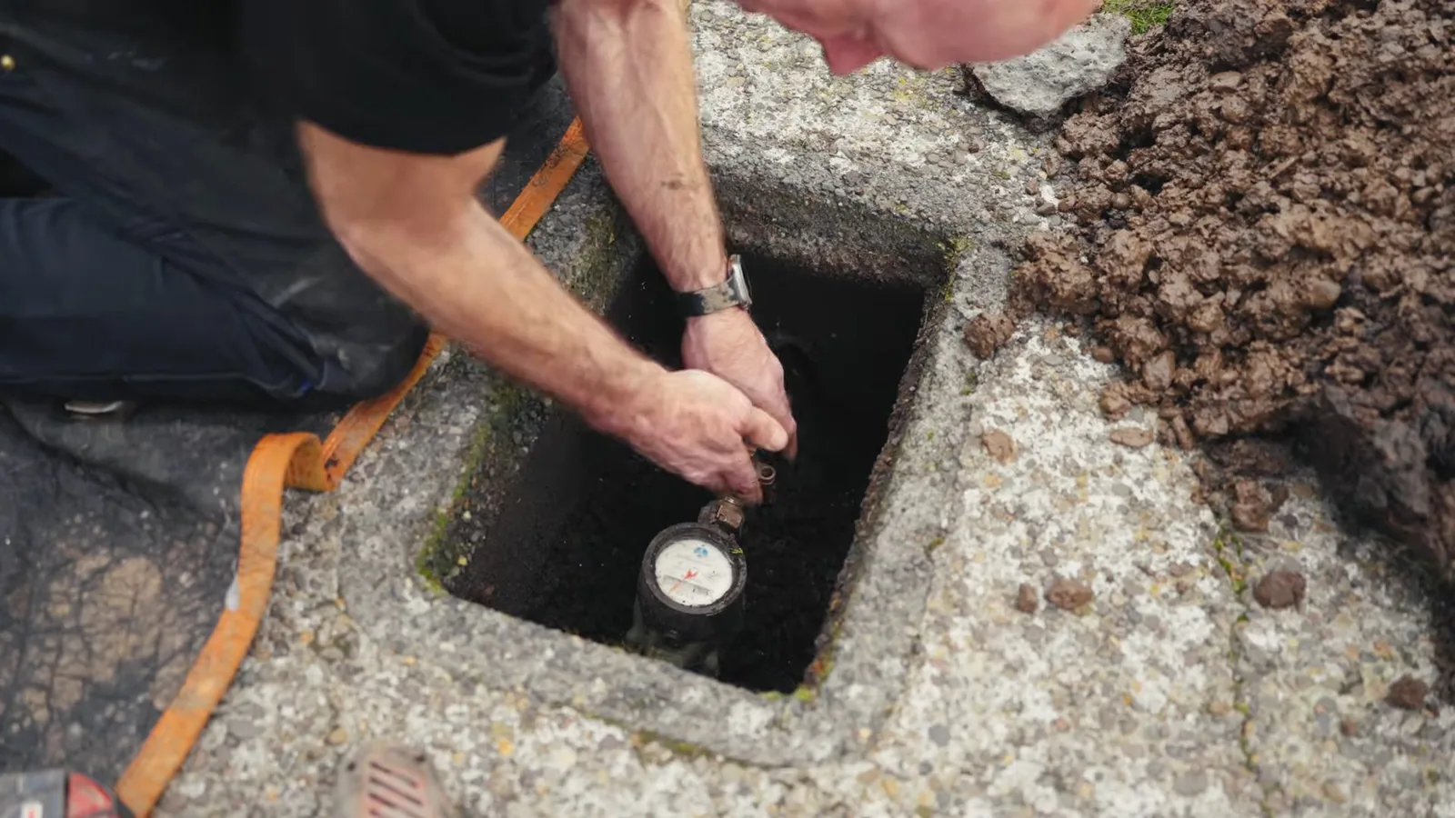A person kneeling beside an open ground-level meter box with both hands on the water meter inside.