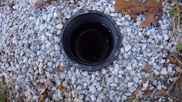 An open black sewer cleanout pipe surrounded by white gravel.