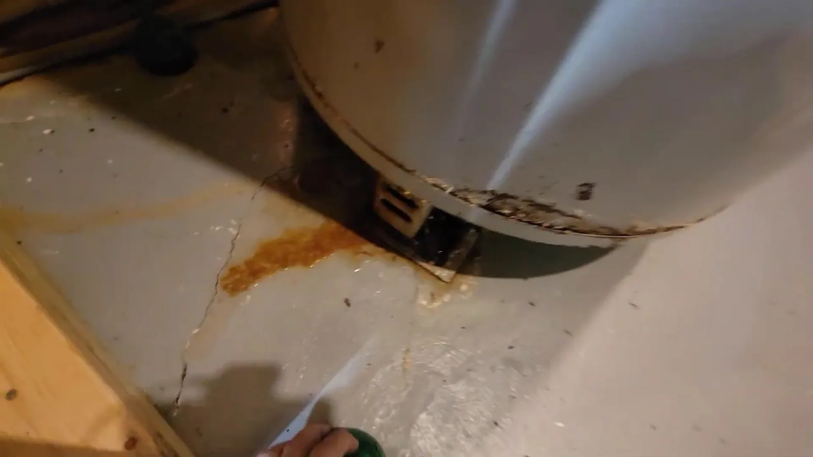 Rust-colored staining on the floor at the base of an older water heater tank.