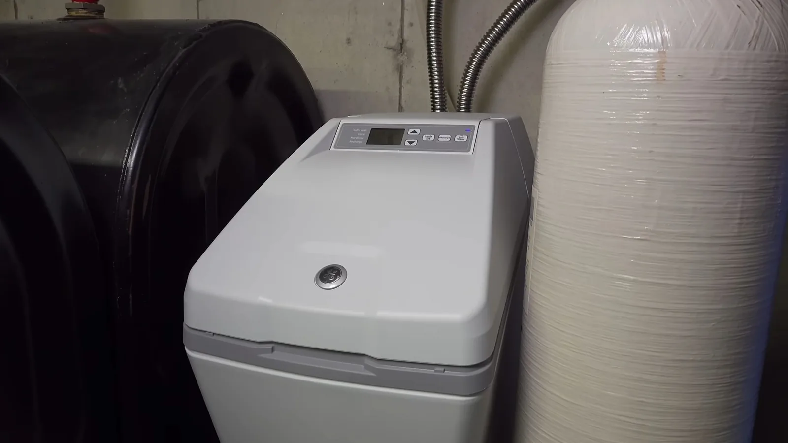 A gray water softener cabinet standing between a black tank on the left and a tall white mineral tank on the right.
